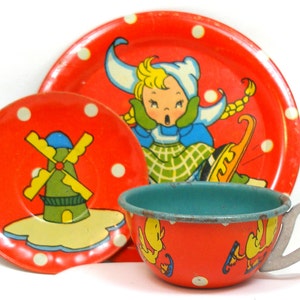 May include: A red and white children's tea set with a windmill and a girl on a sled design. The set includes a teacup, saucer, and a larger plate.