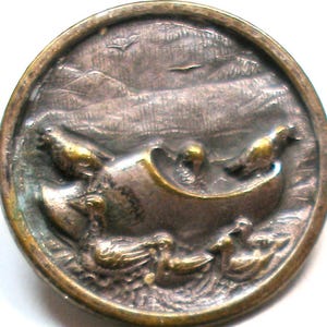 May include: Antique bronze button with a detailed relief of ducks swimming in water, a boat, and birds flying in the sky. The button has a circular shape with a slightly tarnished finish, giving it a vintage appearance.