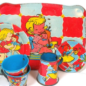 Könnte beinhalten: Ein Vintage-Kinderspielzeug-Tee-Set mit einem rot-blau karierten Tablett. Das Set enthält zwei Tassen, eine Kanne, einen Teller und eine Untertasse. Jedes Stück zeigt eine andere Illustration einer Puppenmädchen mit einem roten, gelben und blauen Farbschema.