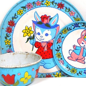 May include: A blue and white children's tea set with a bunny rabbit design. The set includes a cup, saucer, and a larger plate. The plates have a floral border and the cup and saucer have a floral pattern.