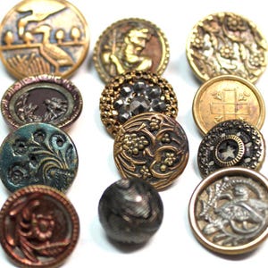 Puede incluir: Una colección de doce botones redondos variados con diversos acabados y texturas metálicas. Los botones muestran intrincados diseños en relieve que incluyen patrones florales, formas geométricas, figuras de animales y un botón esférico oscuro.
