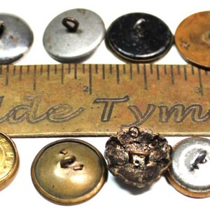 Puede incluir: Una colecci&oacute;n de botones antiguos en varios colores y dise&ntilde;os, incluyendo negro, dorado, plateado y bronce. Una regla de lat&oacute;n con el texto "Olde Tyme Not" se coloca junto a los botones. Los botones var&iacute;an en tama&ntilde;o y estilo.