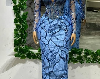 May include: A light blue, floor-length gown with intricate sequin and bead embellishments. The dress features a plunging neckline, long sleeves, and a fitted bodice that flares out at the hips. The dress is displayed on a mannequin.