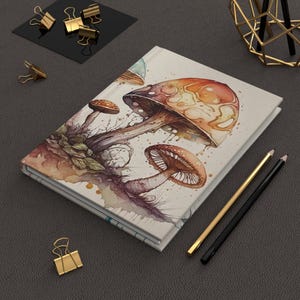 May include: A watercolor notebook cover with a design of mushrooms in shades of brown, orange, and yellow. The mushrooms are painted with a realistic style and have a whimsical feel.