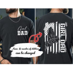 May include: Black t-shirt with the text "Girl Dad" in white block letters. The back of the shirt features a distressed American flag design with a hand-holding graphic and the words "Girl Dad" vertically. The names of the children are also printed on the back.