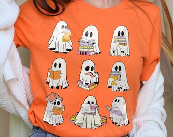 Op de afbeelding: Oranje T-shirt met een afbeelding van negen geesten die boeken lezen. De geesten zijn wit met zwarte ogen en monden. De boeken zijn kleurrijk en in stapels gestapeld.