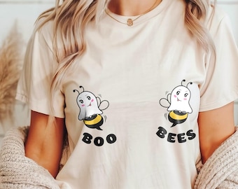 May include: A cream-colored t-shirt with a graphic of two cartoon ghosts dressed as bees. The text "Boo Bees" is printed below the ghosts.