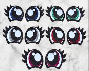 May include: A collection of ten felt eye shapes with glitter accents in various colors, including blue, green, silver, red, and pink. Each eye has a white pupil and black eyelashes, suitable for crafts and DIY projects.