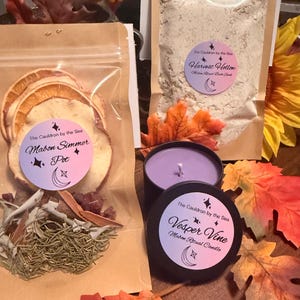 May include: A Mabon Simmer Pot kit with dried fruit and herbs, a Harvest Hollow bath soak, and a Vesper Vine candle in a black tin. The products feature labels from The Cauldron by the Sea with crescent moon and star icons, surrounded by autumn leaves.