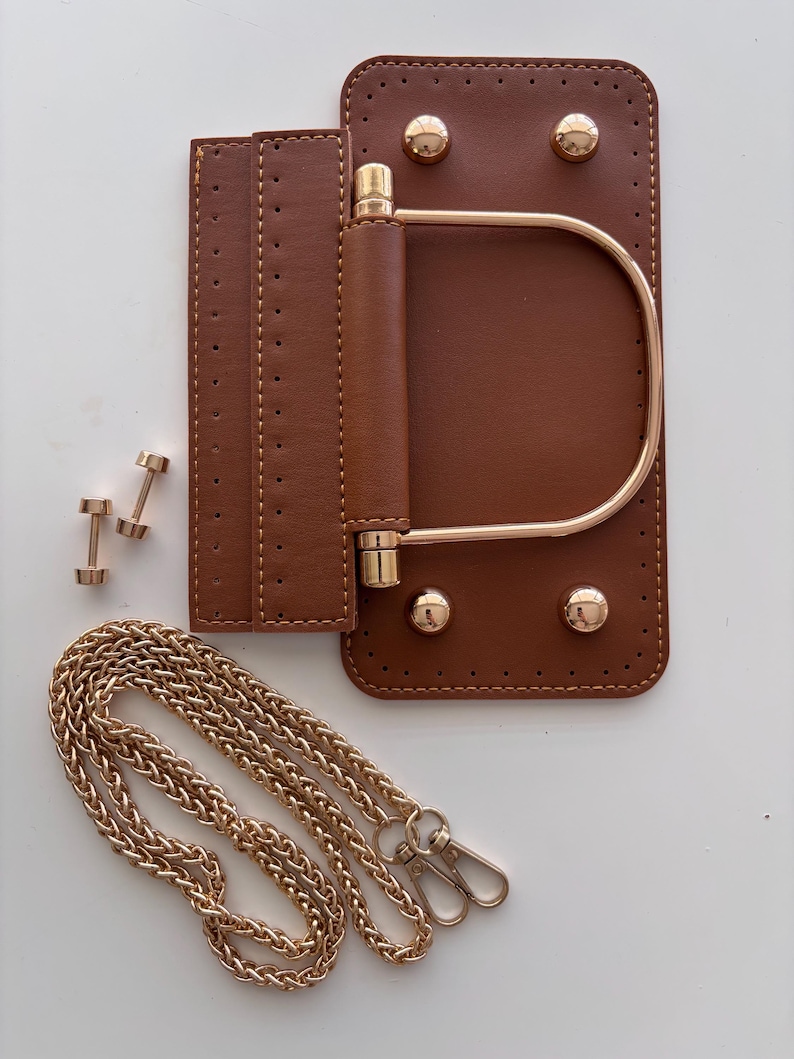 Puede incluir: Componentes de bolso de cuero marr&oacute;n con herrajes dorados. Incluye una base rectangular con esquinas redondeadas, un asa y una correa de cadena. Tambi&eacute;n se muestran dos peque&ntilde;os remaches dorados y una solapa con costuras.