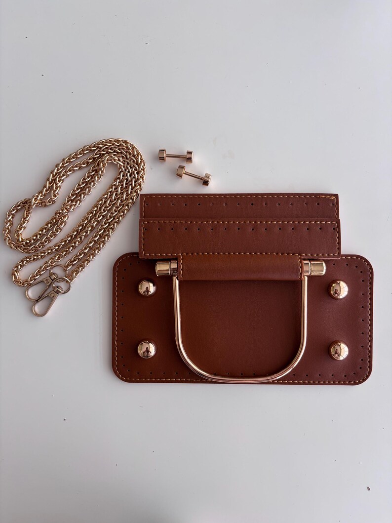 Puede incluir: Base de bolso de cuero marr&oacute;n con asa y tachuelas doradas. Tambi&eacute;n se incluye una cadena dorada y dos tornillos dorados. La base del bolso tiene forma rectangular con un borde cosido.