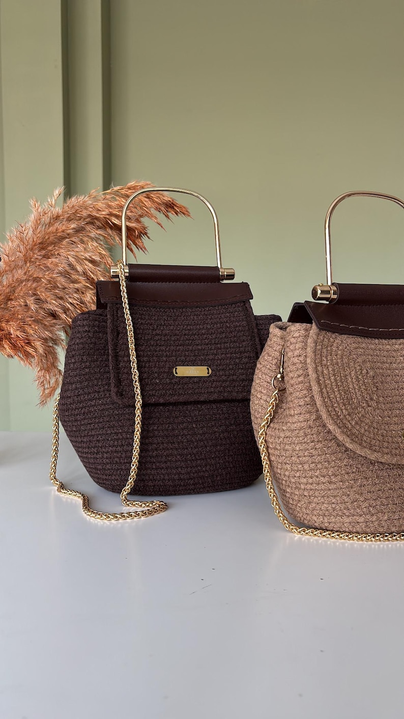Puede incluir: Dos bolsos artesanales. Uno es marr&oacute;n oscuro, el otro es beige. Ambos tienen una textura tejida, correas de cadena doradas y asas doradas. Los bolsos tienen un cierre de solapa con un peque&ntilde;o acento dorado. El fondo es verde claro.