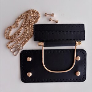 Puede incluir: Un kit negro para hacer bolsos con herrajes dorados. El kit incluye una base rectangular con cuatro tachuelas doradas, un asa a juego, una pieza superior, una correa de cadena dorada y dos peque&ntilde;os conectores dorados. Las piezas est&aacute;n dispuestas sobre una superficie blanca.