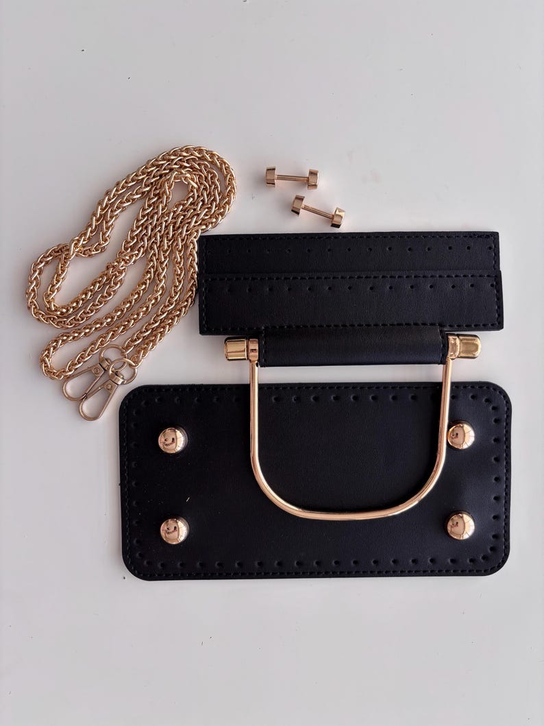 Puede incluir: Un kit negro para hacer bolsos con herrajes dorados. El kit incluye una base rectangular con cuatro tachuelas doradas, un asa a juego, una pieza superior, una correa de cadena dorada y dos peque&ntilde;os conectores dorados. Las piezas est&aacute;n dispuestas sobre una superficie blanca.