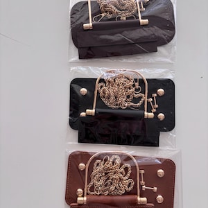 Puede incluir: Tres marcos de bolso en marr&oacute;n, negro y marr&oacute;n oscuro, cada uno con una cadena y un asa doradas. Los marcos son rectangulares con bordes redondeados y est&aacute;n empaquetados en pl&aacute;stico transparente.