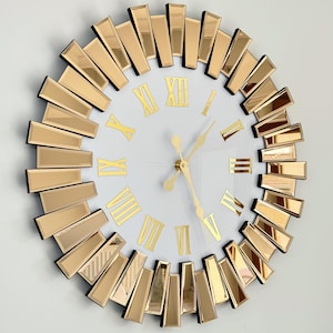 Peut inclure: Une horloge murale en miroir doré avec des chiffres romains et un cadran blanc. L'horloge a un design en forme de soleil avec des carreaux en miroir doré.