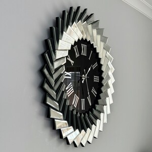 May include: A large, black and silver mirrored clock with Roman numeral markings. The clock face is surrounded by a decorative design of mirrored pieces.