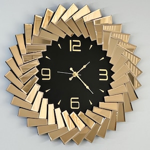Peut inclure: Une grande horloge murale ronde de couleur or avec un cadran noir et des aiguilles des heures et des minutes dorées. L'horloge est entourée d'un cadre décoratif en carreaux de verre miroir.