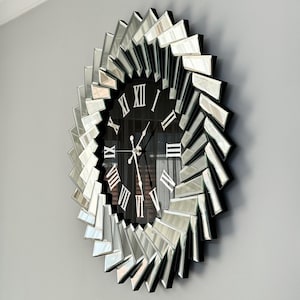 May include: A large, round, mirrored wall clock with Roman numeral markings. The clock face is black with silver hands and a mirrored frame.