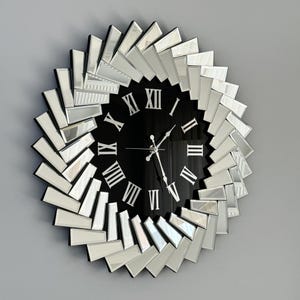 May include: A large, round, mirrored wall clock with a black face and Roman numeral hour markers. The clock has a silver frame with a sunburst design.