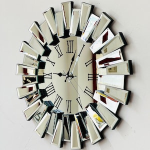May include: A mirrored wall clock with a sunburst design. The clock face has Roman numerals and black hands.