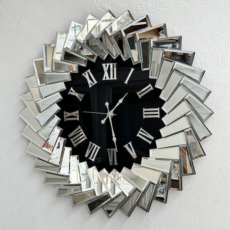 May include: A large, round, mirrored wall clock with Roman numeral markings on a black face. The clock is surrounded by a ring of mirrored tiles arranged in a sunburst pattern.
