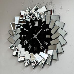 May include: A large, round, mirrored wall clock with Roman numeral markings on a black face. The clock is made of many small, mirrored pieces that are arranged in a sunburst pattern.
