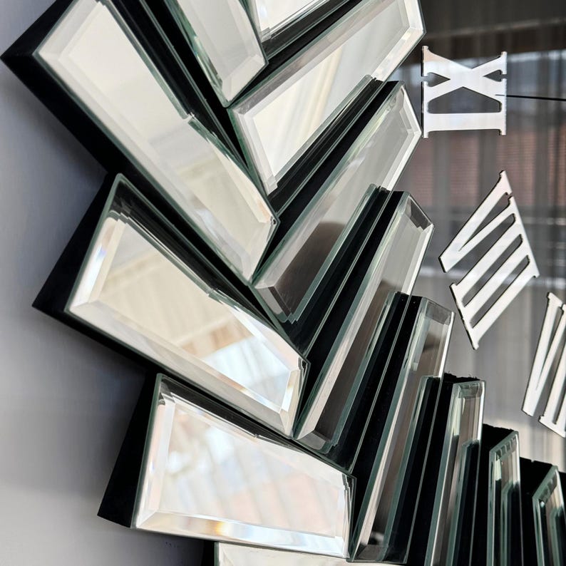 May include: A black and silver mirrored clock with Roman numeral markings. The clock face is made up of multiple mirrored pieces arranged in a sunburst pattern.