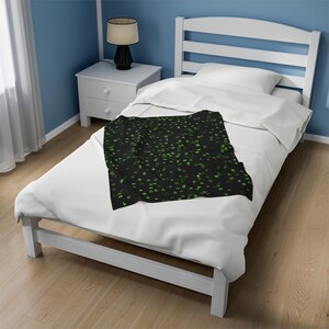 May include: A black throw blanket with a green pattern of various symbols. The blanket is on a white bed with a white headboard.