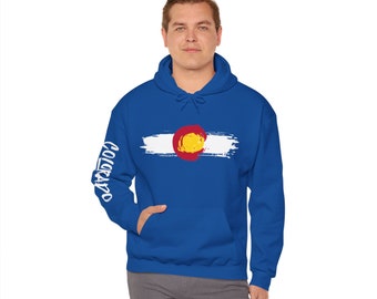 Pode incluir: Um moletom azul royal com um design branco salpicado de tinta da bandeira do estado do Colorado na frente. A palavra "Colorado" está escrita verticalmente na manga esquerda em branco.