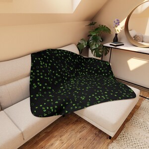 May include: A black throw blanket with a pattern of green symbols. The blanket is draped over a white couch.