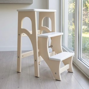 Op de afbeelding: Een tweetraps opstapje met een lichtbeige houten frame, gebogen zijsteunen en vlakke witte treden. De constructie bestaat uit een hoge rugsteun en een lagere trede, verbonden door metalen bevestigingen voor een stabiel en functioneel ontwerp.