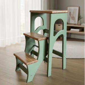 May include: A white ceramic mug with a black handle and the text "But First, Coffee" in a bold, black font. The mug is set against a blurred background, suggesting a cozy setting.