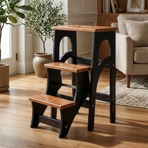 May include: A three-step wooden step stool featuring a black frame with natural wood-toned treads and a top platform. The stool has arched side supports and a rectangular cutout handle on the top step for portability and ease of movement.