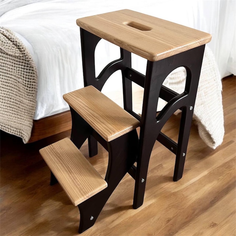May include: A two-step wooden step stool with a light brown top step and two light brown steps. The frame is black. The top step has a handle cutout. The stool is designed for reaching higher places.