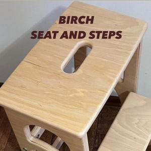 May include: A light-colored birch wood step stool with a rectangular seat and a handle cutout. The text "BIRCH SEAT AND STEPS" is printed on the seat. The stool has a second step below.