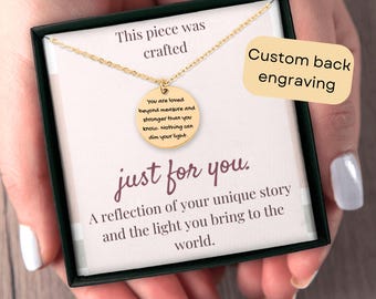 May include: A gold necklace with a round pendant that reads "You are loved beyond measure and stronger than you know. Nothing can dim your light." The pendant is in a black box with a white background and the text "This piece was crafted" and "Custom back engraving" on the box. The text "just for you." is written below the pendant.