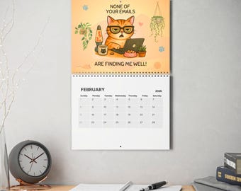 May include: A wall calendar featuring a cartoon cat wearing glasses and working on a laptop. The text reads "NONE OF YOUR EMAILS ARE FINDING ME WELL!" The calendar shows the month of February 2026.
