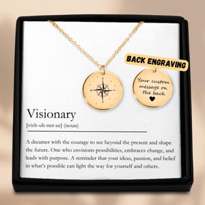 May include: Gold necklace with a compass pendant and a second pendant for engraving a custom message. The necklace comes in a black box with a definition of the word "Visionary".