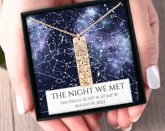 May include: A gold necklace with a rectangular pendant engraved with a star map. The pendant is in a black box with a blue background and white stars. The box has a white label with the text "THE NIGHT WE MET" and the date and location of the event.