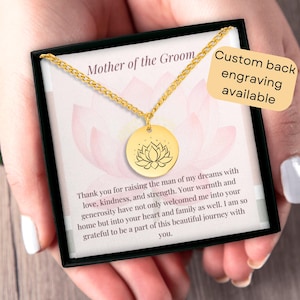 May include: Gold necklace with a lotus flower pendant in a black gift box. The box has a card with the text "Mother of the Groom" and a message of gratitude. The card also says "Custom back engraving available".
