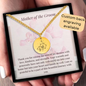 May include: Gold necklace with a round pendant featuring an engraved orchid design. The necklace is in a black box with a message for the mother of the groom. The box also states that custom back engraving is available.