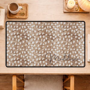 May include: A rectangular desk mat with a brown and white spotted pattern, framed by a black border. The cursive name "Maddison" is printed in the center. The mat is designed for use on a desk.
