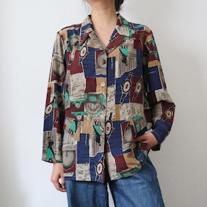 Puede incluir: Una camisa abotonada con un diseño de patchwork colorido. La camisa presenta una mezcla de patrones rectangulares burdeos, azul marino, verde azulado y beige. La camisa de manga larga tiene cuello y está hecha de una tela ligera.