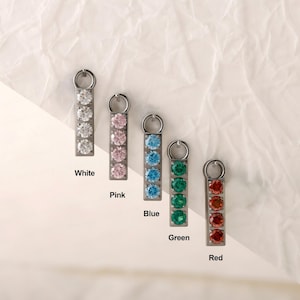 Peut inclure: Cinq pendentifs verticaux en métal, chacun orné de quatre pierres précieuses rondes alignées. Les pendentifs sont étiquetés White, Pink, Blue, Green et Red, correspondant aux pierres transparentes, roses, bleu clair, vertes et rouges.