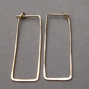 May include: A pair of gold-toned rectangular hoop earrings. The earrings are made of a thin, hammered metal.