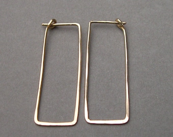 May include: A pair of gold-toned rectangular hoop earrings. The earrings are made of a thin, hammered metal.