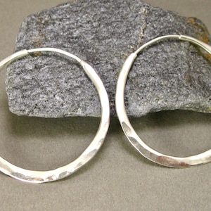 May include: A pair of silver hoop earrings with a hammered finish. The earrings are large and circular in shape.