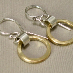 May include: A pair of gold and silver earrings with a circle design. The earrings have a silver hook and a gold circle with a silver band around it.