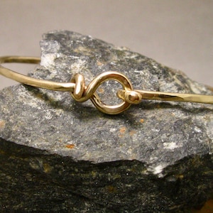 Puede incluir: Un brazalete de oro con acabado martillado y cierre anudado.